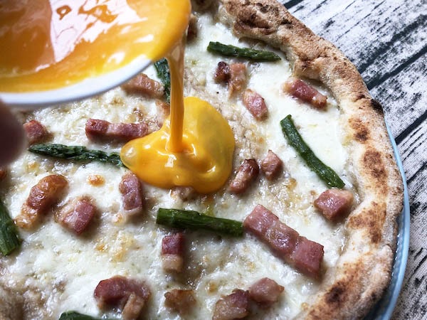 東急ベルSALUSが販売するピッツェリア・ダ・グランツァの冷凍ピザ「ピッツァ・カルボナーラ」に卵黄をかける
